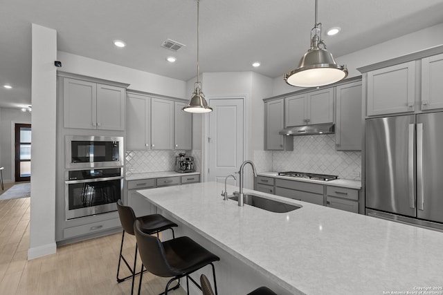 kitchen with pendant lighting, gray cabinets, appliances with stainless steel finishes, a sink, and under cabinet range hood