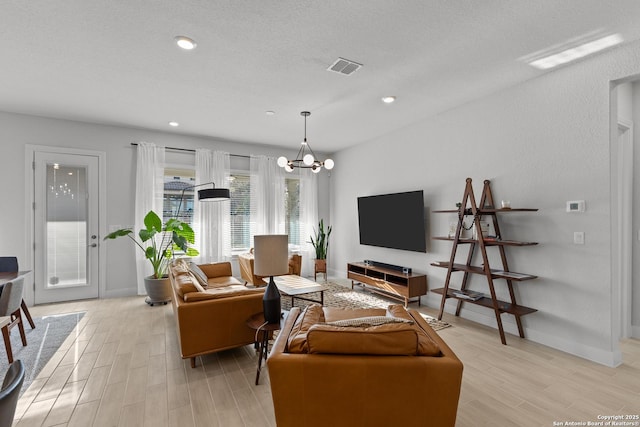 living room featuring light wood-type flooring, an inviting chandelier, visible vents, and a textured ceiling