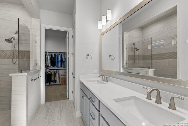 bathroom featuring double vanity, a tile shower, a sink, and a walk in closet