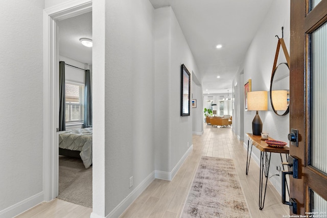 corridor featuring baseboards, light wood finished floors, recessed lighting, and an inviting chandelier