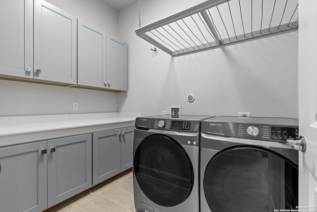 washroom with light wood-type flooring, cabinet space, and washing machine and clothes dryer