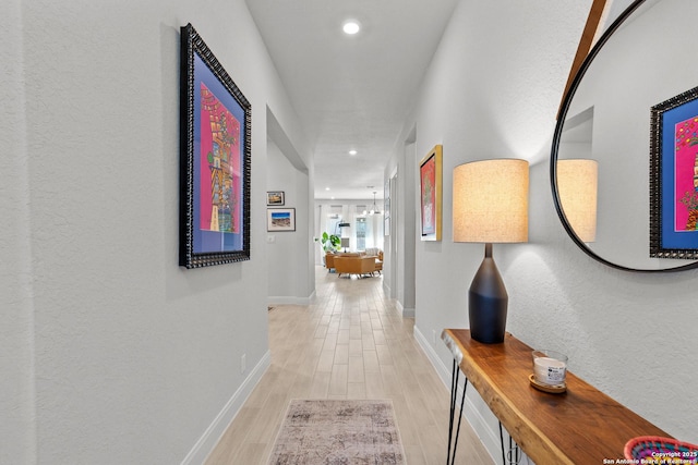 corridor with light wood-style flooring, baseboards, a notable chandelier, and recessed lighting