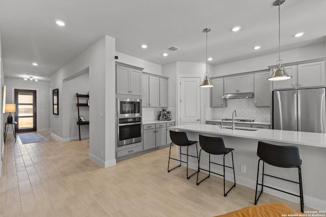 kitchen with stainless steel appliances, visible vents, under cabinet range hood, and a kitchen bar