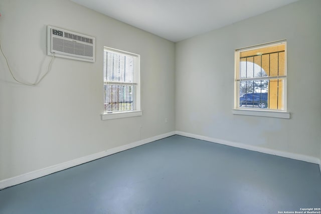 empty room featuring a wealth of natural light, baseboards, concrete flooring, and an AC wall unit