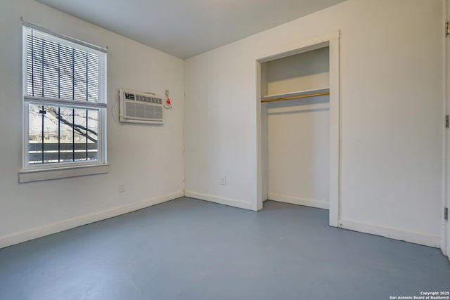 unfurnished bedroom featuring baseboards, a closet, a wall unit AC, and finished concrete floors