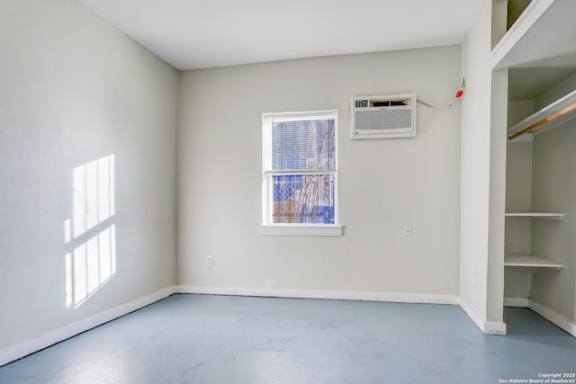 unfurnished room with finished concrete floors, baseboards, and a wall mounted AC