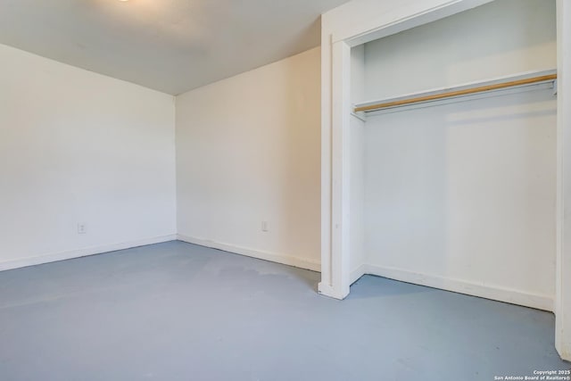 unfurnished bedroom with concrete flooring, a closet, and baseboards