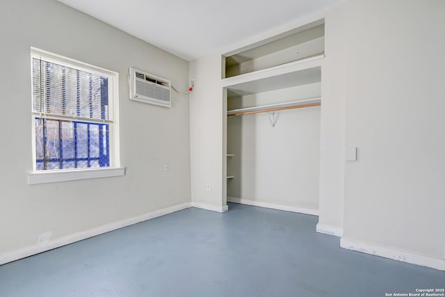 unfurnished bedroom with concrete flooring, a closet, a wall mounted air conditioner, and baseboards