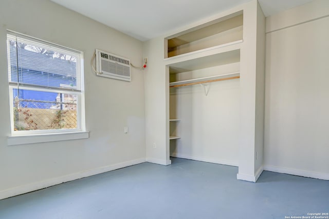 unfurnished bedroom featuring baseboards, a closet, a wall mounted air conditioner, and finished concrete floors