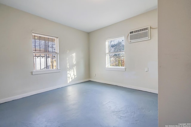 spare room featuring finished concrete flooring, baseboards, and a wall mounted air conditioner