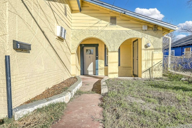 entrance to property featuring brick siding, fence, and stucco siding