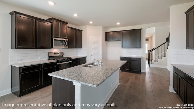 kitchen featuring a kitchen island with sink, light stone counters, stainless steel appliances, and a sink