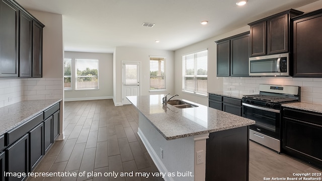 kitchen featuring a center island with sink, stainless steel appliances, visible vents, a sink, and light stone countertops