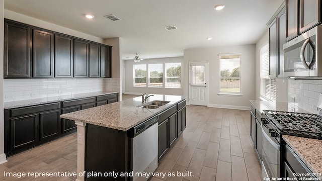 kitchen featuring a sink, visible vents, appliances with stainless steel finishes, light stone countertops, and a center island with sink