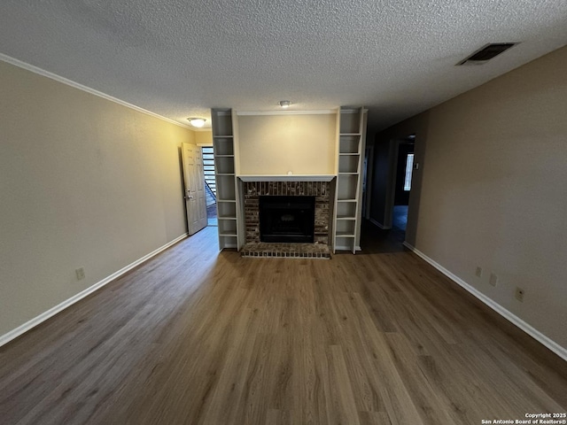 unfurnished living room with a brick fireplace, baseboards, visible vents, and wood finished floors