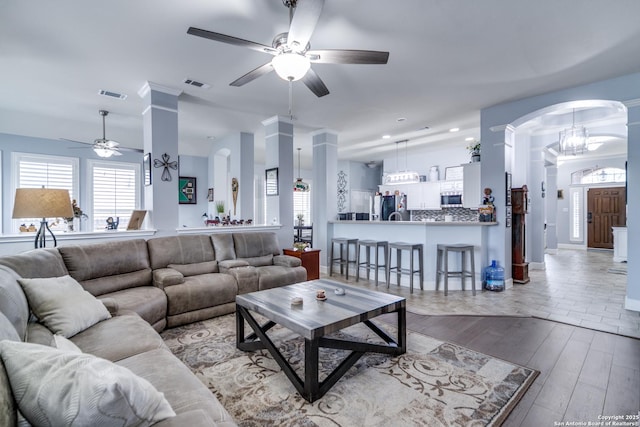 living area with light wood-style floors, visible vents, arched walkways, and a ceiling fan