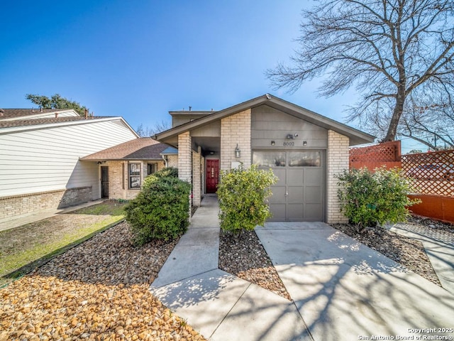 mid-century home featuring a garage, fence, concrete driveway, and brick siding