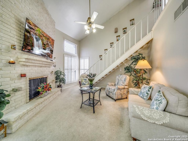 carpeted living room with visible vents, stairway, a ceiling fan, a brick fireplace, and high vaulted ceiling