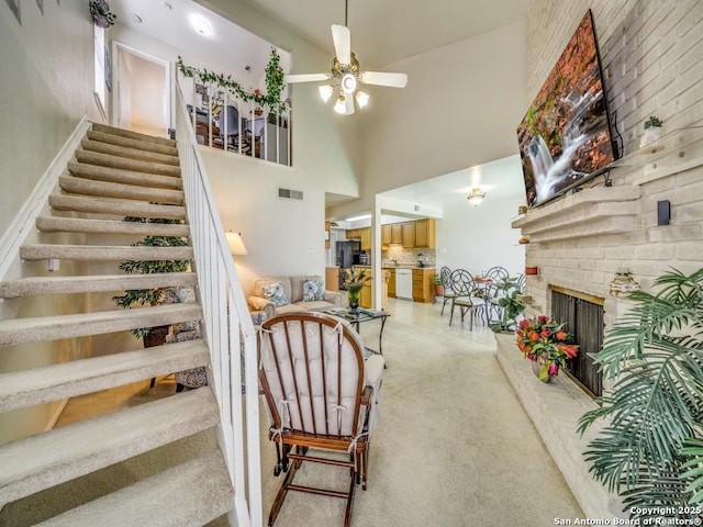 stairs featuring visible vents, a ceiling fan, a towering ceiling, carpet floors, and a fireplace