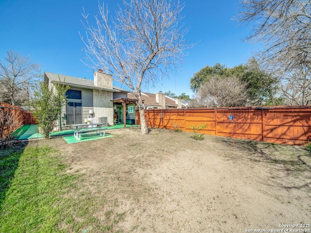 back of property featuring a yard, a fenced backyard, brick siding, and a chimney