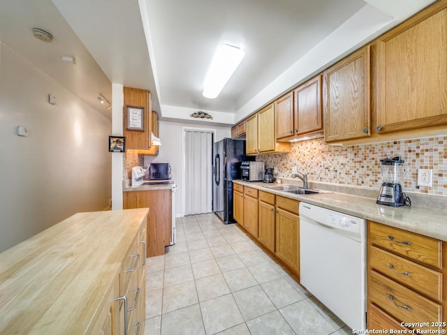 kitchen featuring dishwasher, backsplash, freestanding refrigerator, light countertops, and a sink