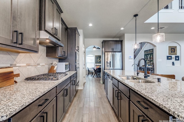 kitchen featuring light stone counters, arched walkways, pendant lighting, appliances with stainless steel finishes, and a sink