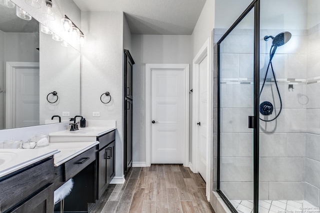 bathroom with double vanity, wood finished floors, a sink, and a shower stall