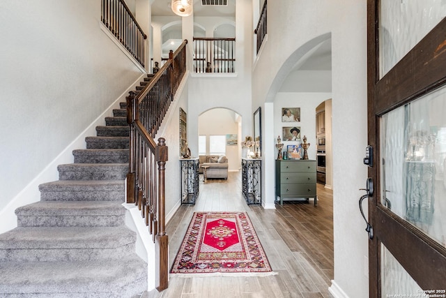 entrance foyer with arched walkways, visible vents, a high ceiling, wood finished floors, and baseboards