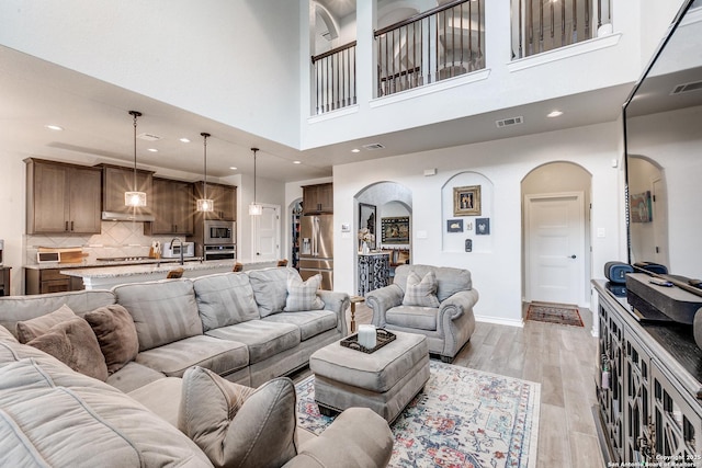 living area featuring arched walkways, light wood finished floors, recessed lighting, visible vents, and baseboards