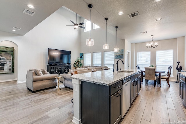 kitchen featuring light stone counters, a sink, visible vents, hanging light fixtures, and an island with sink