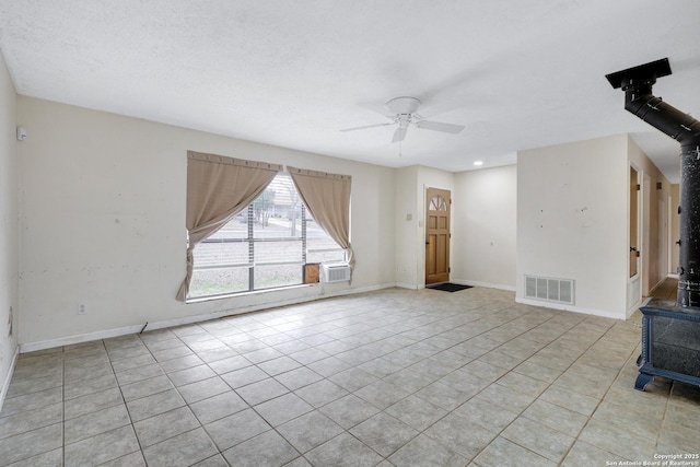 unfurnished living room with light tile patterned floors, visible vents, a wood stove, ceiling fan, and baseboards