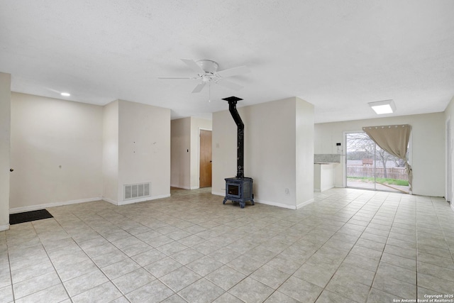 unfurnished living room with baseboards, visible vents, a ceiling fan, a wood stove, and a textured ceiling