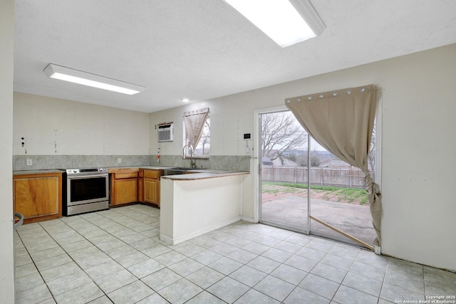 kitchen with light tile patterned floors, brown cabinetry, stainless steel electric stove, light countertops, and a sink