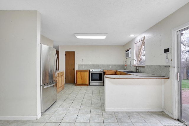 kitchen featuring light tile patterned floors, appliances with stainless steel finishes, a peninsula, light countertops, and a sink