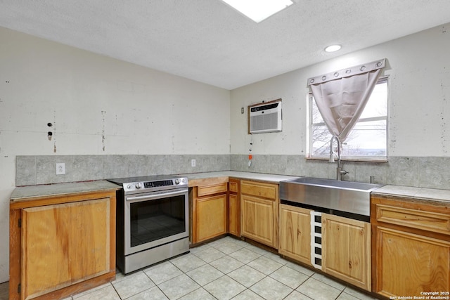 kitchen with light tile patterned floors, light countertops, stainless steel range with electric stovetop, a sink, and a wall mounted AC