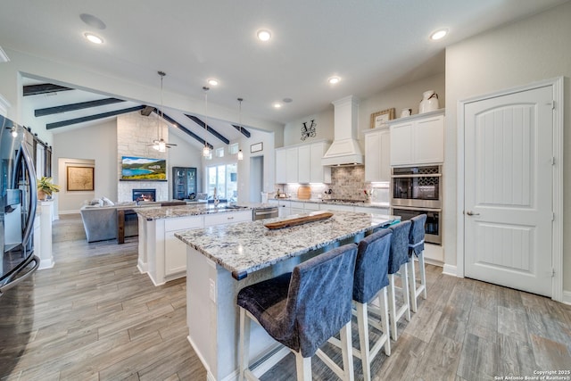 kitchen with white cabinets, open floor plan, custom exhaust hood, a center island, and pendant lighting