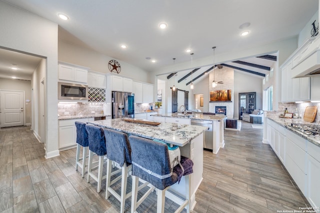 kitchen featuring a spacious island, appliances with stainless steel finishes, white cabinets, light stone countertops, and a kitchen breakfast bar