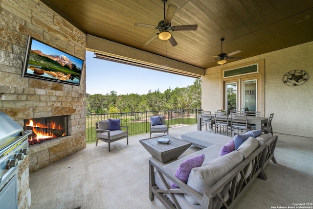 view of patio / terrace featuring a wooded view, outdoor dining space, an outdoor living space with a fireplace, and a ceiling fan