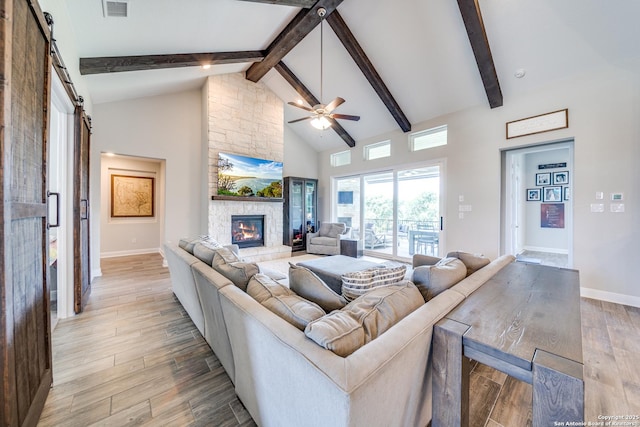 living room with high vaulted ceiling, a barn door, a fireplace, light wood-type flooring, and beamed ceiling