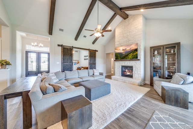 living room with a barn door, visible vents, light wood-style flooring, a fireplace, and high vaulted ceiling