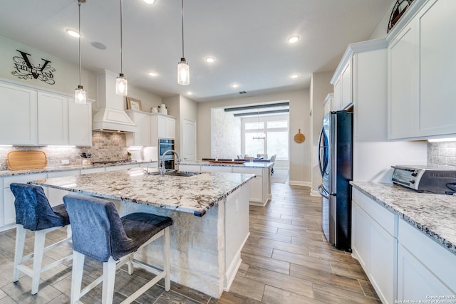 kitchen with stainless steel appliances, premium range hood, an island with sink, and white cabinetry