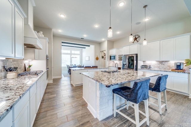 kitchen featuring white cabinets, appliances with stainless steel finishes, a center island with sink, and light stone countertops