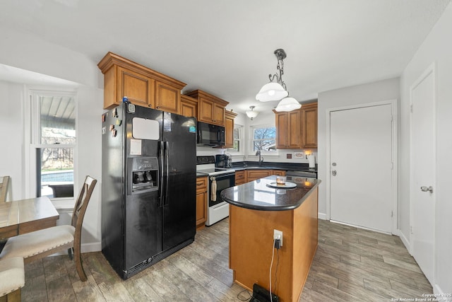 kitchen featuring a center island, hanging light fixtures, brown cabinets, black appliances, and dark countertops