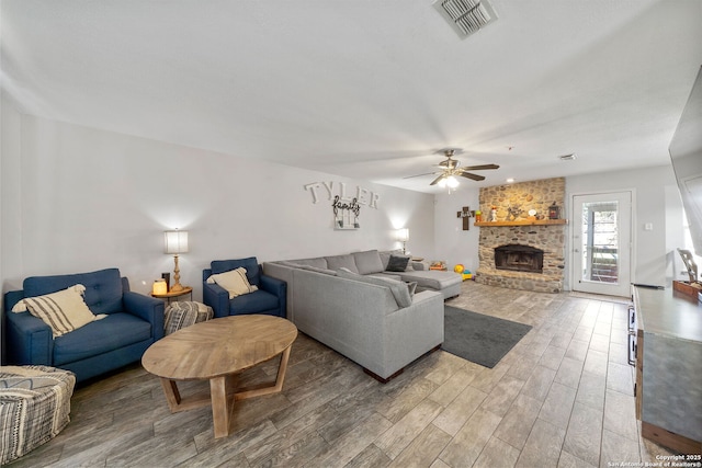 living area featuring ceiling fan, a brick fireplace, wood finished floors, and visible vents