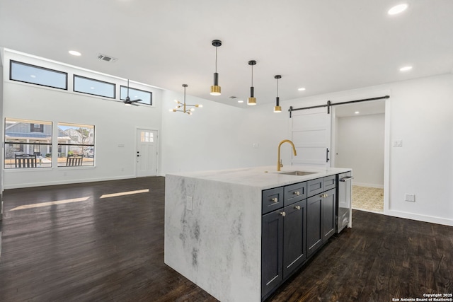 kitchen featuring decorative light fixtures, a center island with sink, a barn door, a sink, and light stone countertops