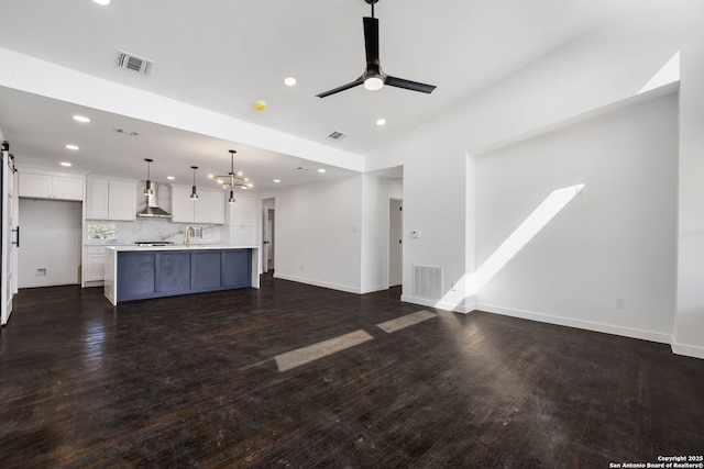 unfurnished living room with ceiling fan with notable chandelier, dark wood-type flooring, visible vents, and baseboards