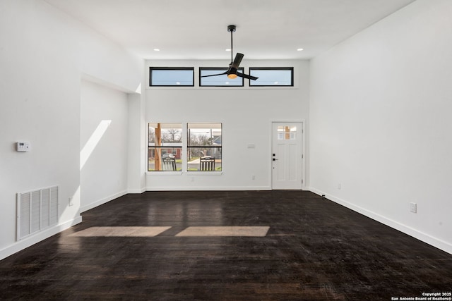 unfurnished living room featuring ceiling fan, a towering ceiling, visible vents, baseboards, and dark wood finished floors