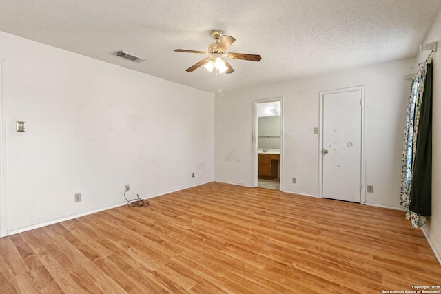 unfurnished bedroom featuring a textured ceiling, ensuite bathroom, visible vents, and light wood-style floors