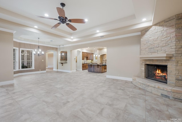 unfurnished living room featuring arched walkways, a stone fireplace, a raised ceiling, and baseboards