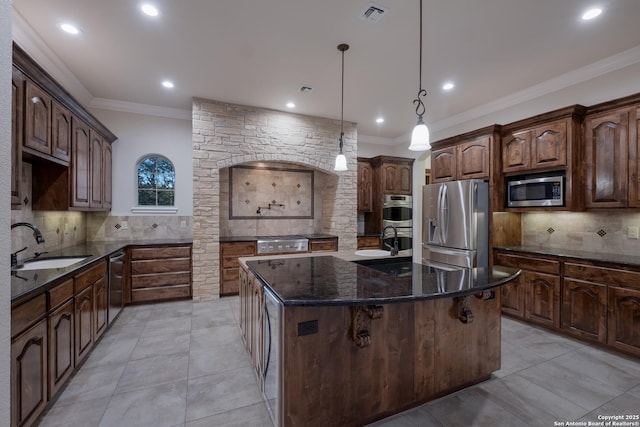 kitchen featuring decorative light fixtures, stainless steel appliances, visible vents, a sink, and an island with sink